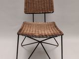 une chaise en osier marron avec des pieds en métal noir et une assise en osier