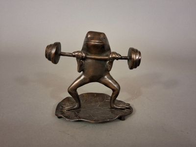une statue représentant une grenouille soulevant une barre d'haltères posée sur un disque