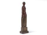 statue d'une femme debout sur un socle en bois, les mains dans les poches