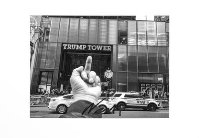 black and white photograph of a person holding up a peace sign in front of a trump tower