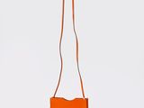 un sac à main orange muni d'une longue bandoulière qui pend sur le côté
