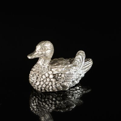 un gros plan d'une figurine de canard en argent posée sur une surface noire