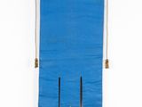 an old blue cloth hanging on a white wall with a wooden pole
