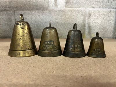 quatre clochettes en laiton vieilli posées sur une table, près d'un mur de briques