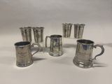 quatre tasses en métal argenté et quatre verres posés sur un plan de travail blanc