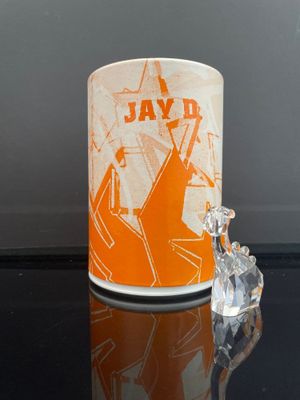 bougeoir en céramique orange et blanche, orné d'une figurine en cristal posée sur un fond noir