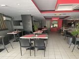 Dans un restaurant aux murs rouges, des tables et des chaises sont alignées.