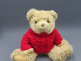 a teddy bear wearing a red sweater sitting on a gray surface