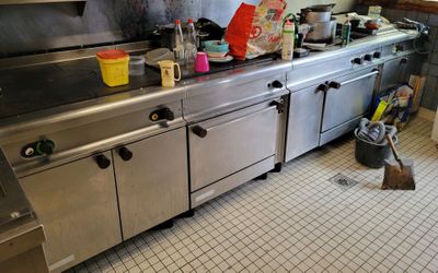 une grande cuisine en inox avec un plan de travail encombré