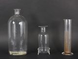 three glass vases and a glass bottle on a black surface