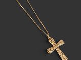 a gold cross pendant with a chain on a black background