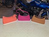 three different colors of purses sitting on a table next to a motorcycle