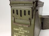 an old green metal box with a metal lid sitting on a white surface
