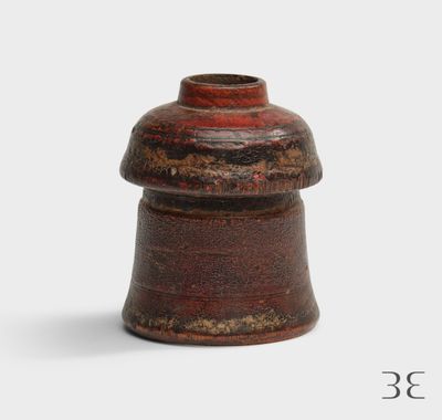 un vase marron surmonté d'un couvercle rouge, posé sur une surface blanche