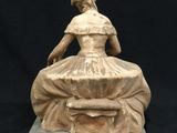 statue of a woman sitting on a rock with a hat on her head