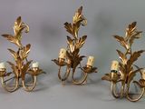 three gold metal wall sconces with flowers and candles on them