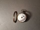 a silver pocket watch sitting on a table next to a ring