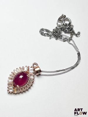 une chaîne en argent avec un pendentif orné d'une pierre rouge, posée sur un fond blanc