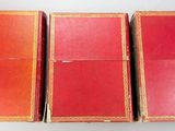 three red books are lined up in a row on a white surface