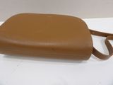 tan leather handbag on a white table with a white background