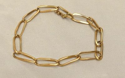un gros plan d'un bracelet à chaîne en or posé sur un tissu blanc