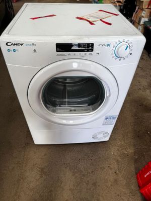 une machine à laver blanche dans un garage, avec un objet rouge posé par terre