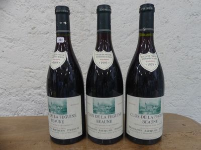 Trois bouteilles de vin rouge sont posées sur une table en bois devant un mur blanc.