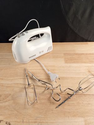 un batteur à main blanc posé sur une table en bois, à côté d'autres ustensiles de cuisine