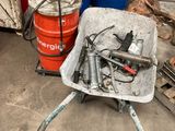 une brouette contenant tout un tas d'outils, à côté de quelques tonneaux