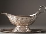 a silver gravy on a silver plate on a gray surface
