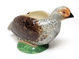 a ceramic bird on a green base with a white background
