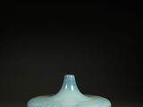 un vase bleu posé sur une table, devant un fond noir