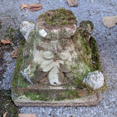 une statue recouverte de mousse, posée par terre au milieu de la rue