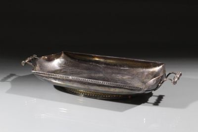 une assiette en argent antique avec une poignée sur une surface blanche
