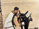 une vieille photo d'un homme caressant un âne dans le désert