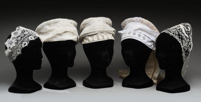 quatre têtes de mannequins coiffées de chapeaux en dentelle, exposées sur un fond gris