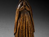 une vieille statue en bois représentant une femme, les mains croisées