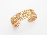 un gros plan d'un bracelet manchette en or sur fond blanc