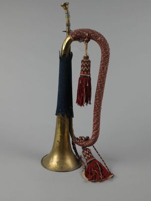 une vieille cloche en laiton à laquelle est suspendu, au niveau du col, un pompon rouge et bleu