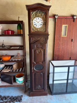 une horloge de parquet dans un coin de la pièce, à côté d'une étagère sur laquelle sont posés des casseroles et des poêles