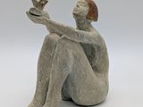 statue of a woman sitting on a white surface holding a bird