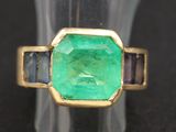 un gros plan d'une bague sertie d'une émeraude verte entourée de saphirs bleus