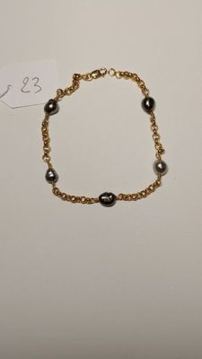a gold bracelet with black pearls on a gold chain
