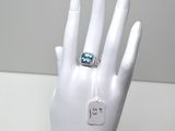 une main de mannequin blanche ornée d'une bague bleue