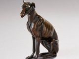 statue en bronze représentant un chien assis sur ses pattes arrière, la gueule ouverte