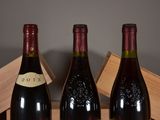 three bottles of wine sit on a wooden crate in front of a gray wall