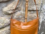 brown leather purse hanging on a stone wall next to a wooden pole