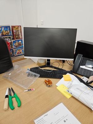a desk with a computer, keyboard, phone, and other items on it