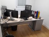 a desk with two computer monitors and a trash can in front of it
