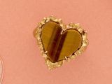 une broche en forme de cœur posée sur un fond rose, à côté d'autres objets